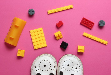 Childhood concept. Children's sandals, toy bricks on pink background. Top view