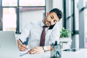 Obraz premium selective focus of concentrated businessman talking on smartphone and using laptop