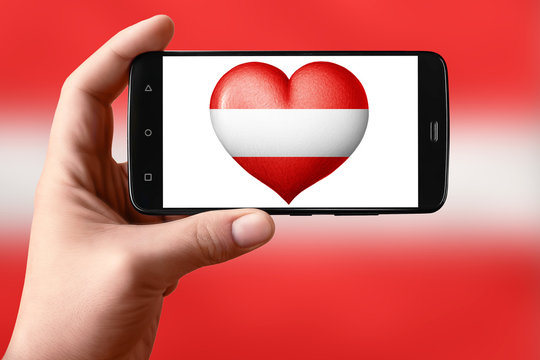 Austria flag in the shape of a heart on the phone screen. Smartphone in hand shows a heart flag.