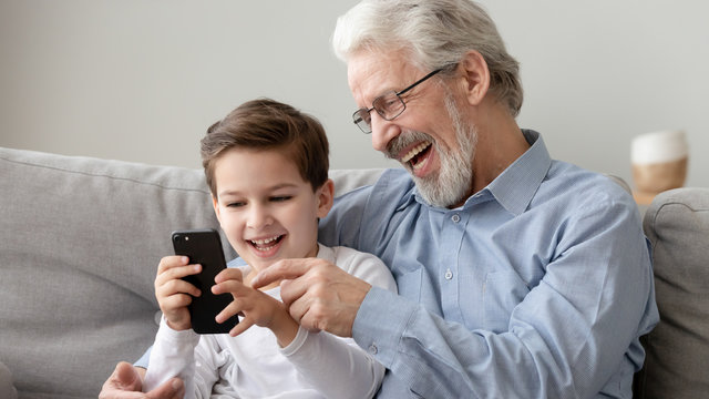 Happy grandfather and little grandson using phone, have fun together