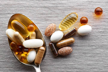 Close-up tablespoon filled with various dietary supplements, tablets and vitamins on a gray fabric...