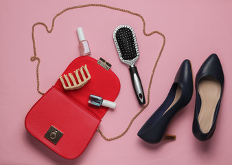 What's in women bag. Red leather bag with women's accessories, cosmetics products, high heel shoes on pink background. Minimalistic fashion concept. Studio shot