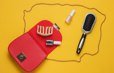 What's in women bag. Red leather bag with women's accessories, cosmetics products on yellow...