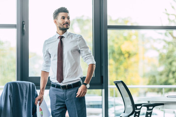 Fototapeta premium handsome businessman holding documents and looking away in office