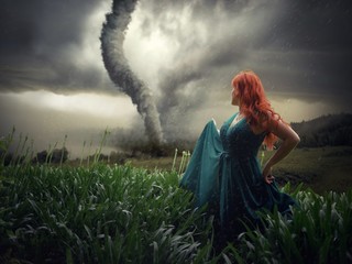Beautiful female standing on a field with a tornado in the background captured in the storm