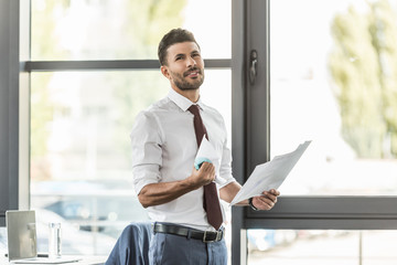Fototapeta premium upset businessman holding documents and crumpling paper while looking away in office