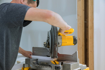Worker cuts wood baseboard on the power saw
