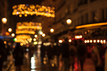 Fototapeta na wymiar Blurry photo of Montorgueil street in Paris at night with beautiful Christmas lights decoration and unrecognizable crowd. Winter holidays vacation and travel concept. Festive urban blurry background.