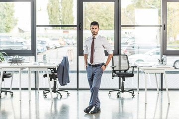 young, confident businessman standing in modern office and looking at camera