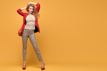 Fashionable woman in Trendy red outfit, stylish wavy hair, makeup. Joyful lady in jacket smiling dance on orange. Cheerful girl, stylish fashion red heels, accessories, beauty style