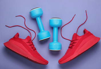 Red sport running shoes with untied laces and dumbbells on purple background. Fitness concept. Top view