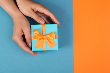 Female holding gift box on blue and orange background. Top view, copy space. Bithday gift. Greeting card with present