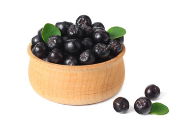 Chokeberry in wooden bowl with green leaves isolated on white background. Black aronia.