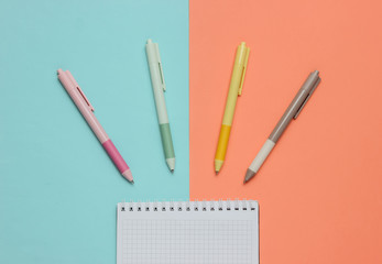 A lot of colored pens with notebook close-up on blue pink background. Top view