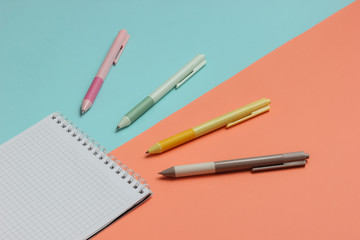 A lot of colored pens with notebook close-up on blue pink background.