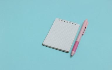 Pink pen with notebook close-up on blue background. Pastel color trend