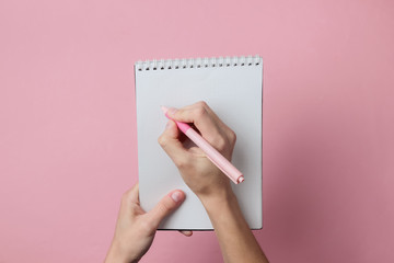 Female hands write with a pen in a notebook on a pink background. Girl's diary. Pastel color trend