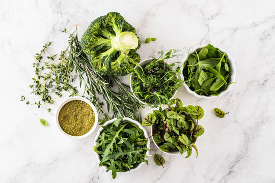 Fresh Green Vegetables Variety On White Background From Overhead, Broccoli, Thyme, Rosemary, Spinach, Microgreens.