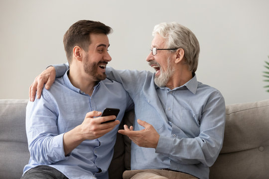 Happy old father and son having fun, using phone together