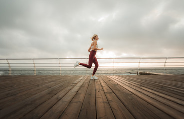 Morning run. Young athletic woman in sportswear runs on the beach at sunrise. Outdoor workout. Healthy lifestyle