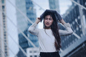 Girl in the heavy rain storm cover head with newspaper for economic obstacle passing concept. - obrazy, fototapety, plakaty
