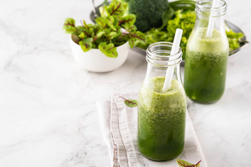 Blended green smoothie with ingredients on the white table.