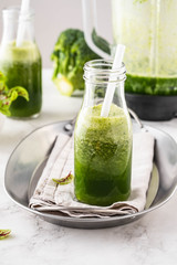 Blended green smoothie with ingredients on the white table.