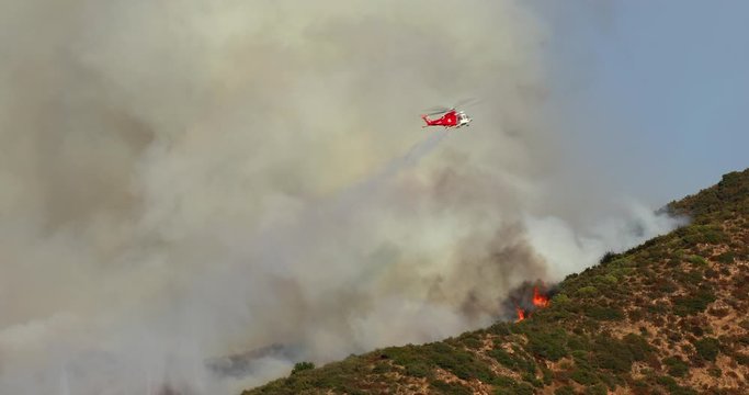 The dramatic view of destroying wildfire on Hollywood hills, near the Warner Bros studio. The hillside forest is in fire. Firefighting helicopter is involved in extinguishing a fire.