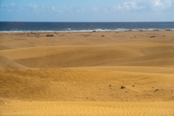 Fototapeta na wymiar Amazing sand dunes during sunny and windy day in the Natural Reserve of Dunes of Maspaloma in Gran Canaria with sand dust and ocean in background, Canary Islands, Spain