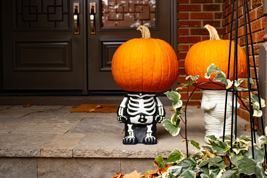 Two pumpkin-heads on small skeleton Halloween cute sculpture standing at the front doors outside of the fancy home. Season outdoor decoration