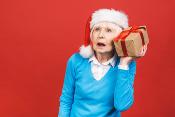 Happy mature woman with a gift. Isolated over red background. Beautiful stylish senior lady opening her Christmas gift. Elegant mature woman holding a red gift box.