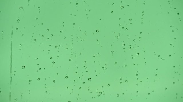 Close up view of water drops falling on green color window glass.
