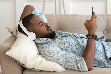 Biracial man relax on sofa listening to music on cellphone
