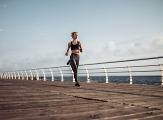 Morning run. Young athletic woman in sportswear runs on the beach at sunrise. Outdoor workout. Healthy lifestyle