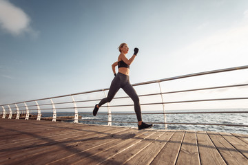 Morning run. Young athletic woman in sportswear runs on the beach at sunrise. Outdoor workout. Healthy lifestyle