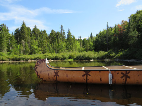 Canadian rabaska canoe resting by the calm water in beautiful  Wapizagonke lake. Mauricie National Park, Quebec Canada.Look out point with blue sky and tranquil waters landscape