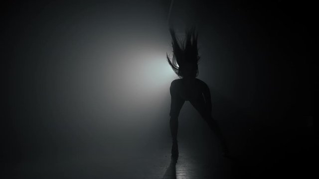 Silhouette of beautiful dancer on smoky dark background.Spotlight shines back against sexy girl. She moving seductively.