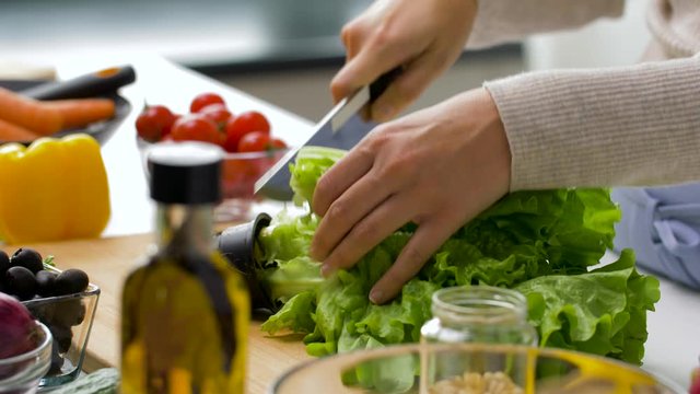 healthy eating, vegetarian food and cooking concept - woman adding lettuce to salad bowl at home kitchen