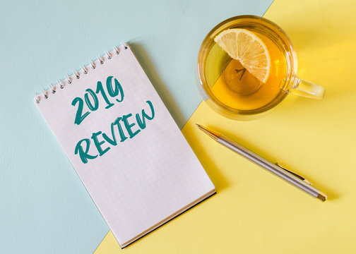 2019 review. Notebook with pen and cup of tea on the blue and yellow background