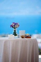 wedding canapes table with white tablecloth glass napkin holder with white napkin centerpiece with bouquets white and purple flowers appetizer olives and french fries blue sea background
