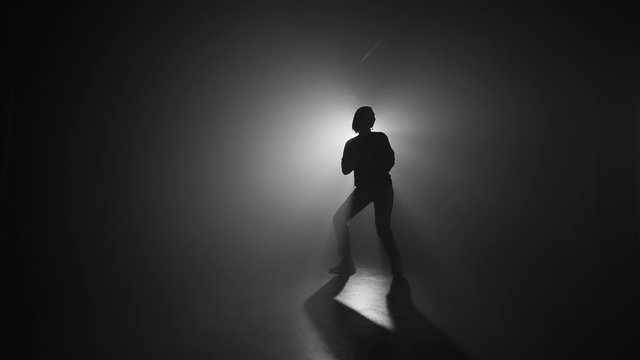 Slim sexy woman dancing on smoke dark stage in front of light projector. Concept of arts, flexibility, talented girl.