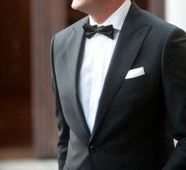 man with tuxedo in motion white shirt black bow tie black jacket and white scarf background in green and terracotta colors