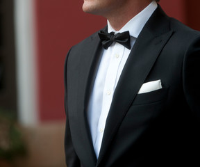 man with tuxedo in motion white shirt black bow tie black jacket and white scarf background in green and terracotta colors