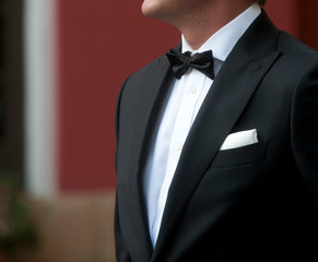 man with tuxedo in motion white shirt black bow tie black jacket and white scarf background in green and terracotta colors