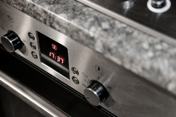 Isolated view of a modern electric oven showing the central digital display. The oven is turned on and the retractable knobs are seen in the on position.  