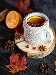Knitted mug of traditional winter and autumn drink mulled wine or sangria on the table with dry autumn leaves, orange, cinnamon and anise