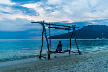 Fototapeta premium Teluk Keke Beach, Besur, Perhentian Islands, Malaysia; 17-May-2019; a lady enjoying a swing by the sea at sunset, Teluk Keke Beach, Besur, Perhentian Islands, Malaysia