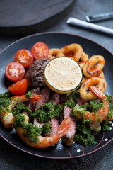 Close-up of surf and turf with marbled beef meat, shrimps, calamari rings, tomatoes and chumuchurri, vertical shot
