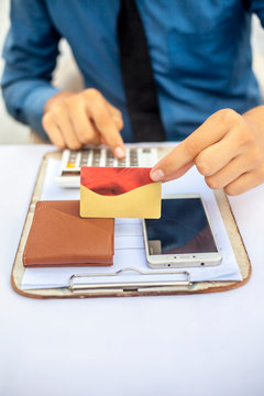 Close up of financial advisor and accountant working on his desk with a calculator and a card in his hand along with his cell phone on the table. In blue corporate clothes.