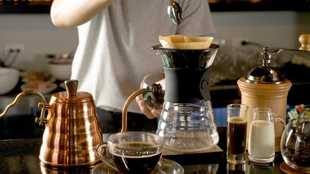Hand drip coffee, Barista making drip coffee by pouring spills hot water on coffee ground with prepare filter from copper  teapot to glass transparent chrome drip maker. on wooden table cafe shop.